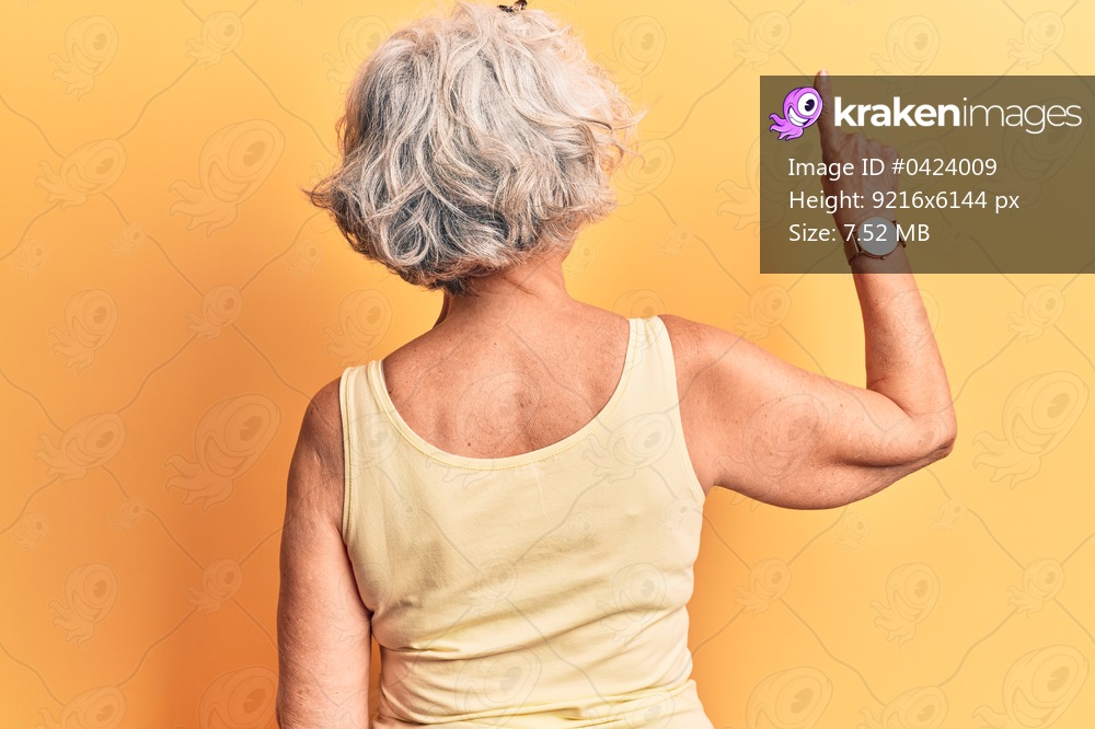 Senior grey-haired woman wearing casual clothes posing backwards pointing ahead with finger hand 