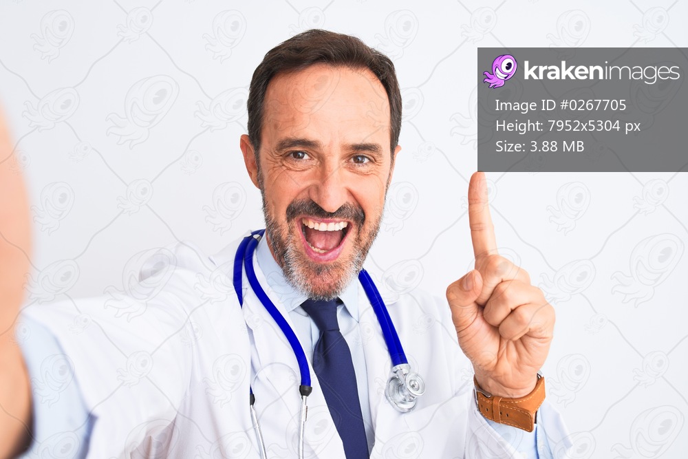 Middle age doctor man wearing stethoscope make selfie over isolated white background surprised with an idea or question pointing finger with happy face, number one