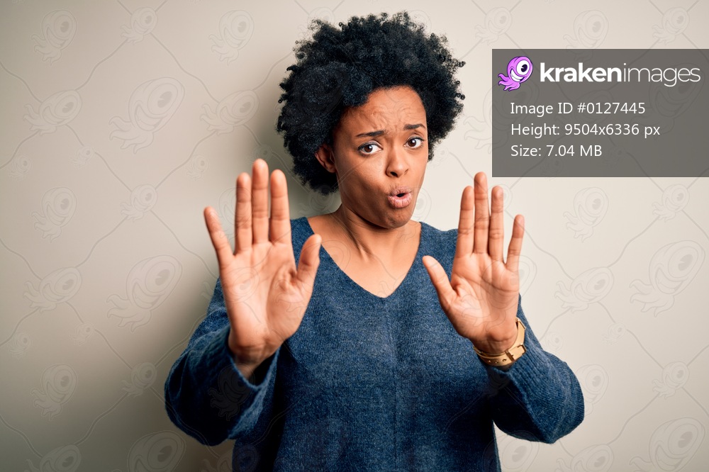 Young beautiful African American afro woman with curly hair wearing casual sweater Moving away hands palms showing refusal and denial with afraid and disgusting expression. Stop and forbidden.