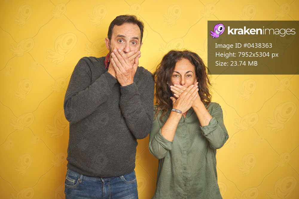 Beautiful middle age couple over isolated yellow background shocked covering mouth with hands for mistake. Secret concept.
