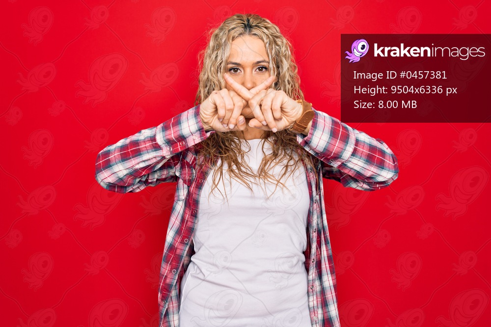 Young beautiful blonde woman wearing casual shirt standing over isolated red background Rejection expression crossing fingers doing negative sign