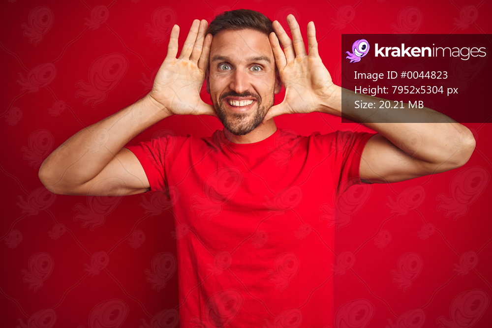 Young handsome man wearing casual t-shirt over red isolated background Smiling cheerful playing peek a boo with hands showing face. Surprised and exited