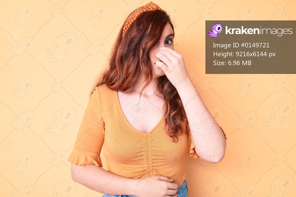 Young beautiful woman wearing casual clothes smelling something stinky and disgusting, intolerable smell, holding breath with fingers on nose. bad smell 