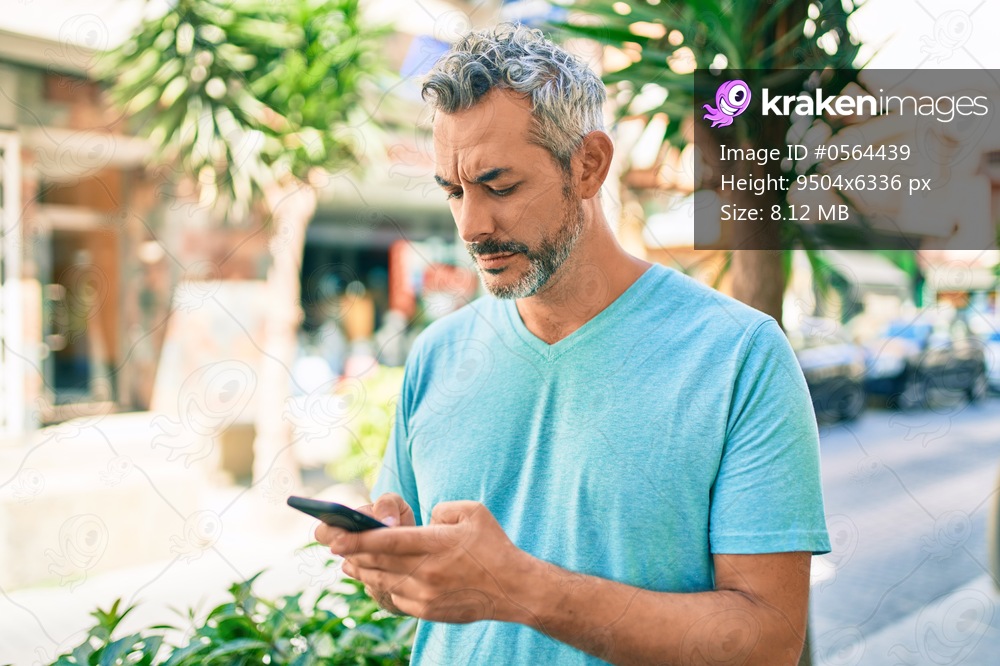 Middle age grey-haired man using smartphone at street of city thinking attitude and sober expression looking self confident 