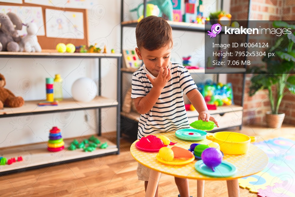 Beautiful toddler boy playing meals with plastic plates, fruits and vegetables at kindergarten