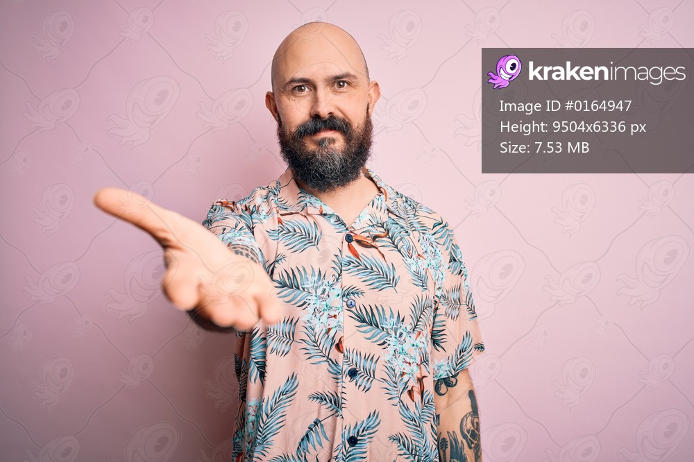 Handsome bald man with beard and tattoo wearing casual floral shirt over pink background smiling cheerful offering palm hand giving assistance and acceptance.