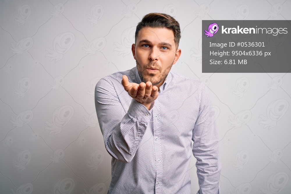Young business man with blue eyes standing over isolated background looking at the camera blowing a kiss with hand on air being lovely and sexy. Love expression.