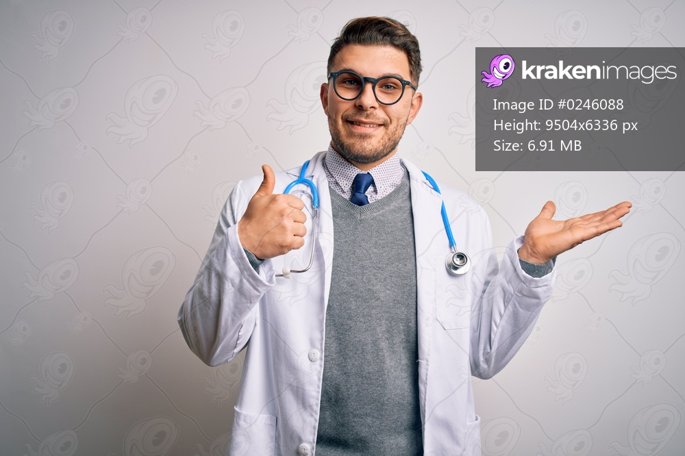 Young doctor man with blue eyes wearing medical coat and stethoscope over isolated background Showing palm hand and doing ok gesture with thumbs up, smiling happy and cheerful
