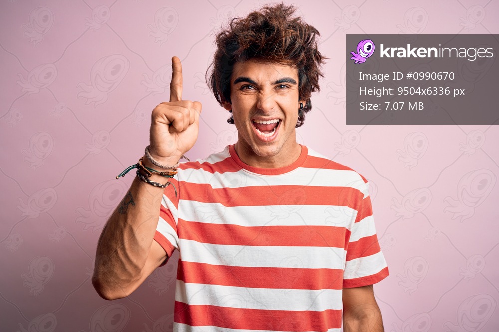 Young handsome man wearing striped casual t-shirt standing over isolated pink background pointing finger up with successful idea. Exited and happy. Number one.