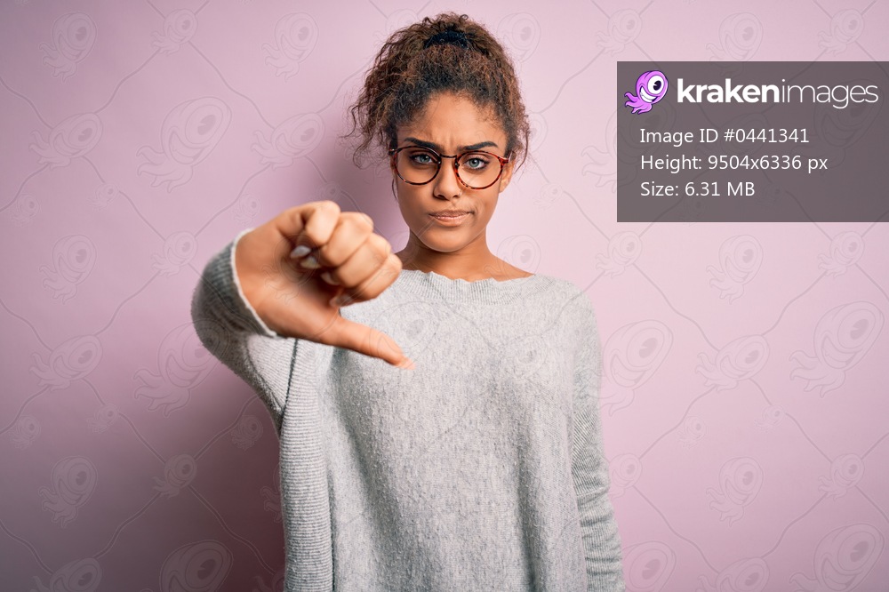 Young beautiful african american girl wearing sweater and glasses over pink background looking unhappy and angry showing rejection and negative with thumbs down gesture. Bad expression.