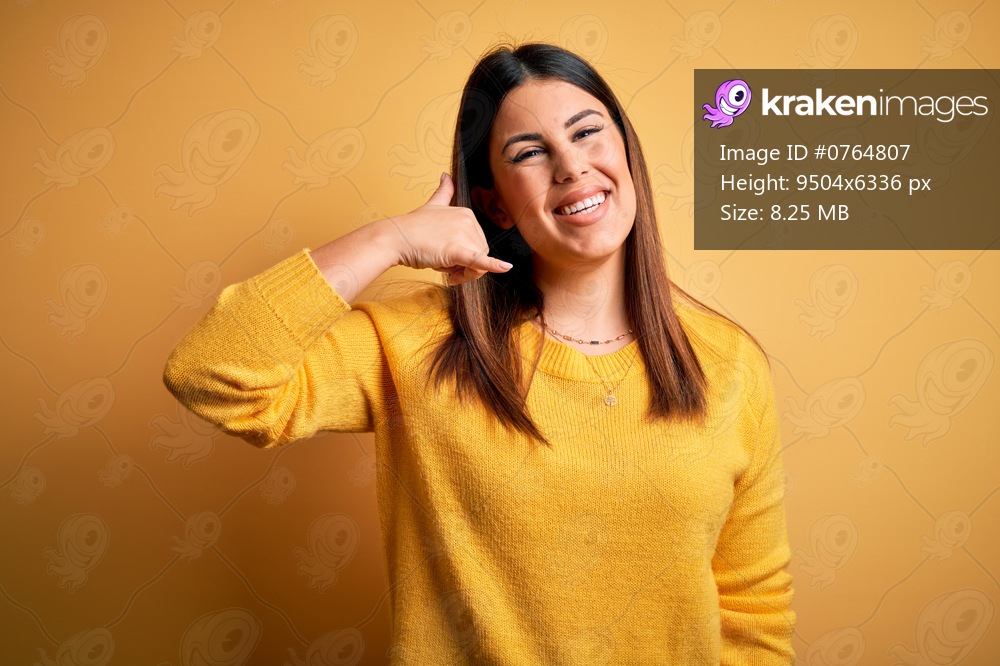 Young beautiful woman wearing casual sweater over yellow isolated background smiling doing phone gesture with hand and fingers like talking on the telephone. Communicating concepts.