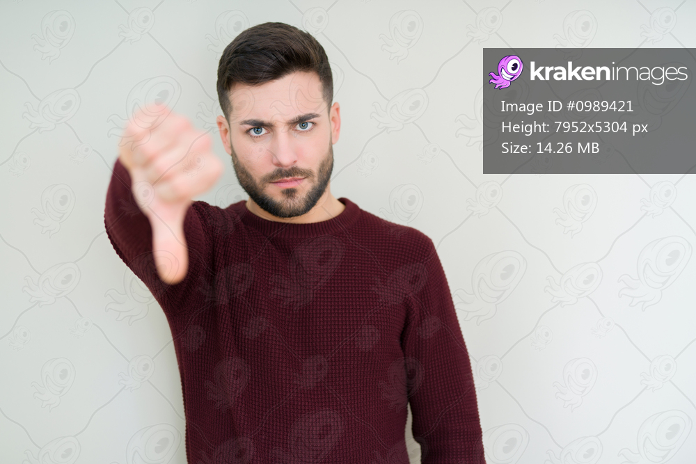 Young handsome man wearing a sweater over isolated background looking unhappy and angry showing rejection and negative with thumbs down gesture. Bad expression.