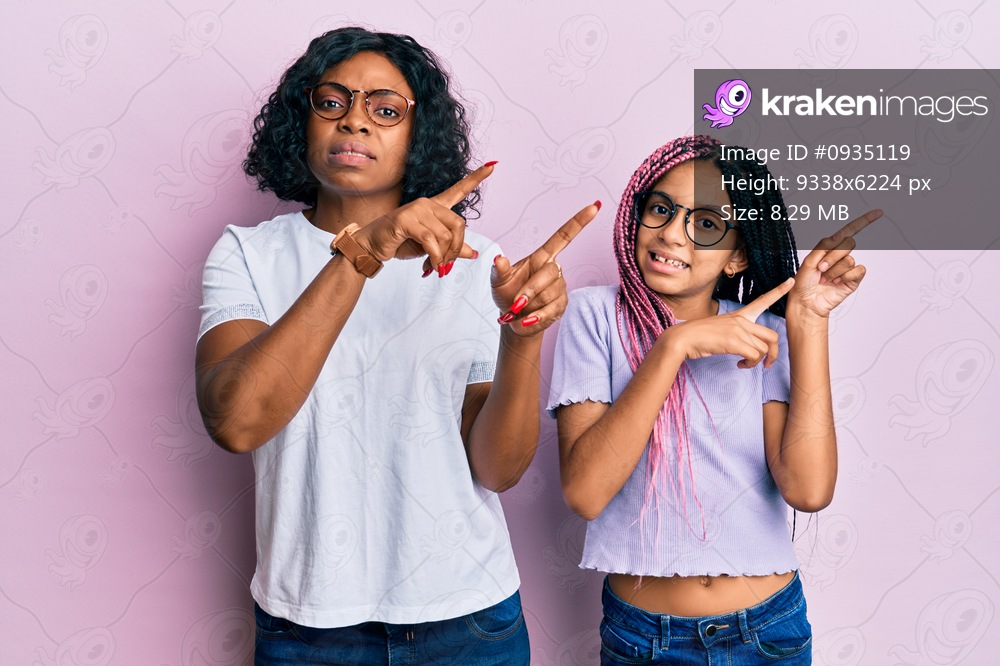 Beautiful african american mother and daughter wearing casual clothes and glasses pointing aside worried and nervous with both hands, concerned and surprised expression 