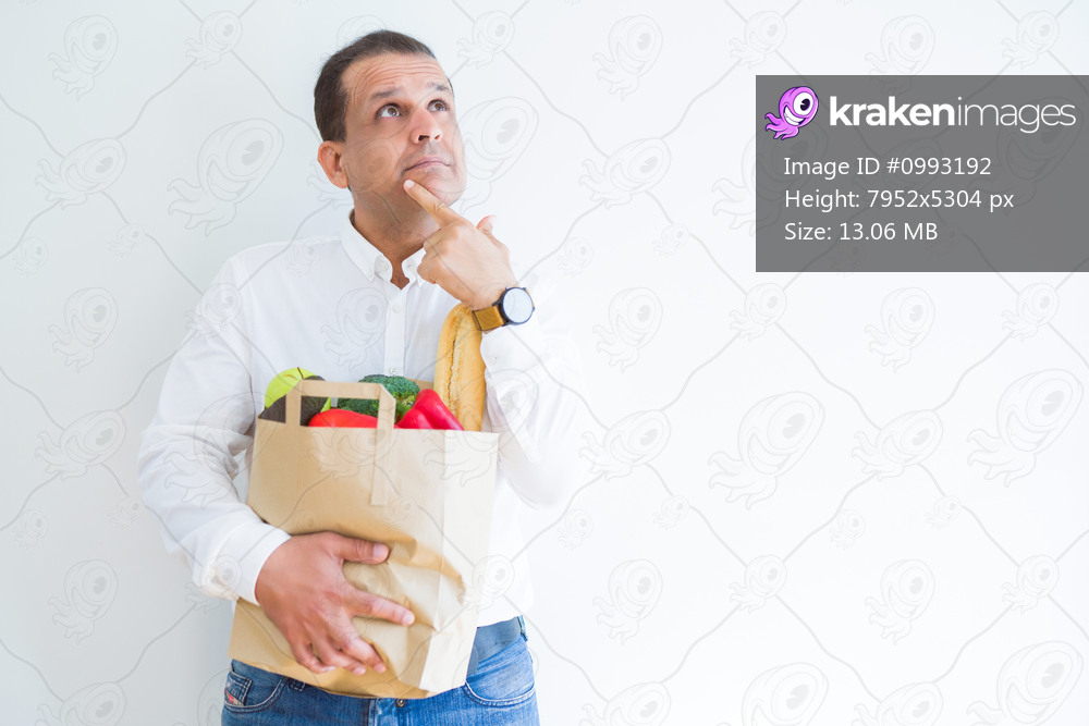 Middle age man holding groceries shopping bag over white background serious face thinking about question, very confused idea