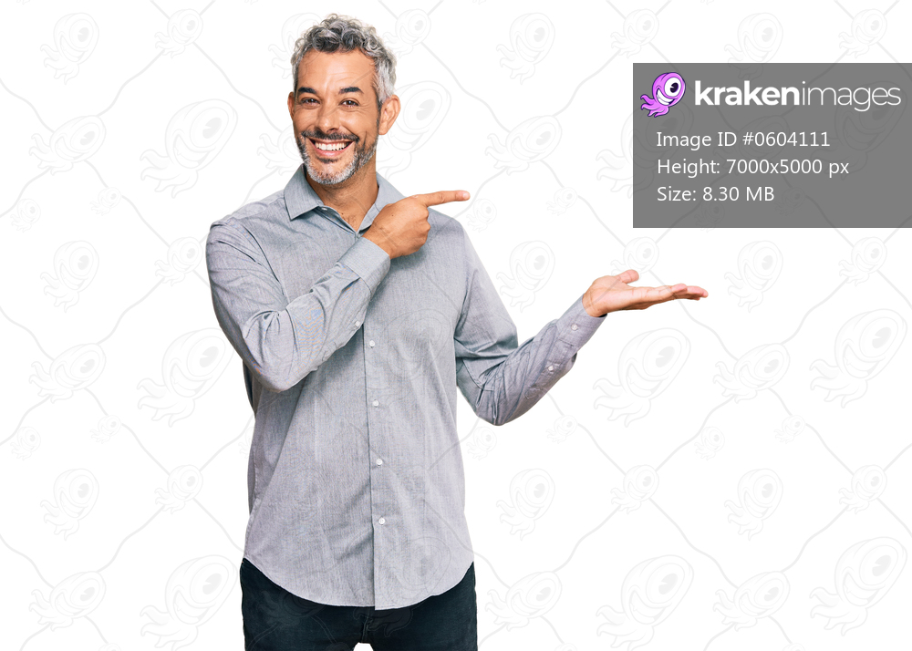 Middle age grey-haired man wearing casual clothes amazed and smiling to the camera while presenting with hand and pointing with finger. 