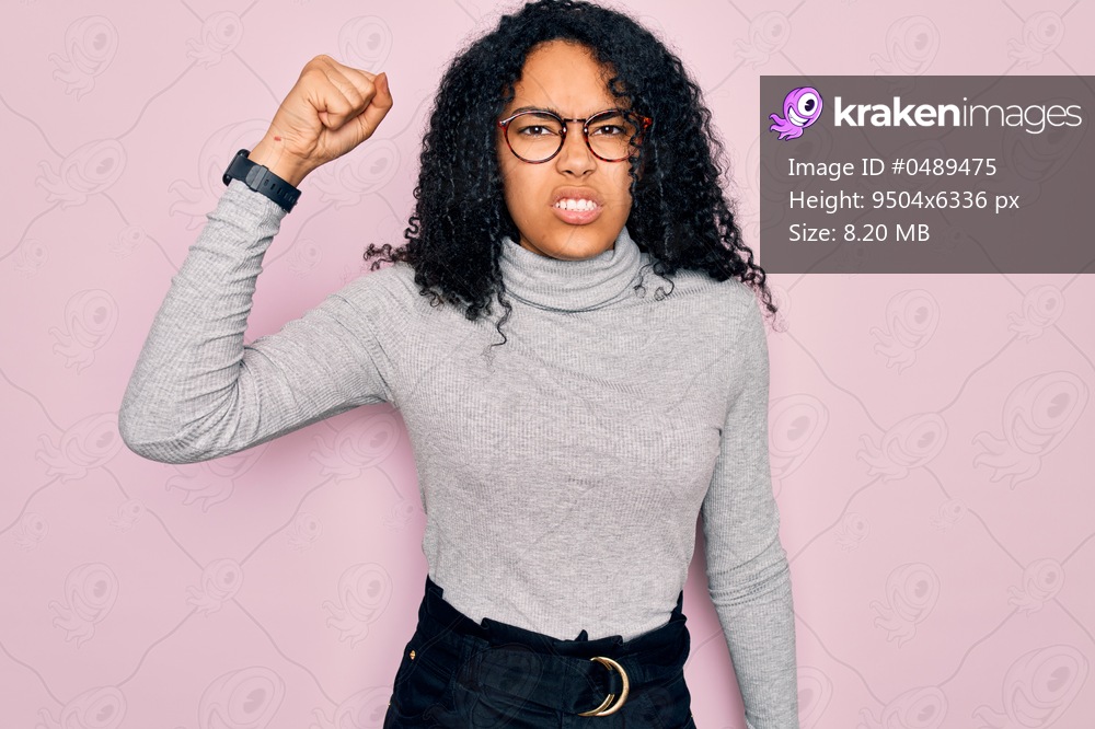 Young african american woman wearing turtleneck sweater and glasses over pink background angry and mad raising fist frustrated and furious while shouting with anger. Rage and aggressive concept.