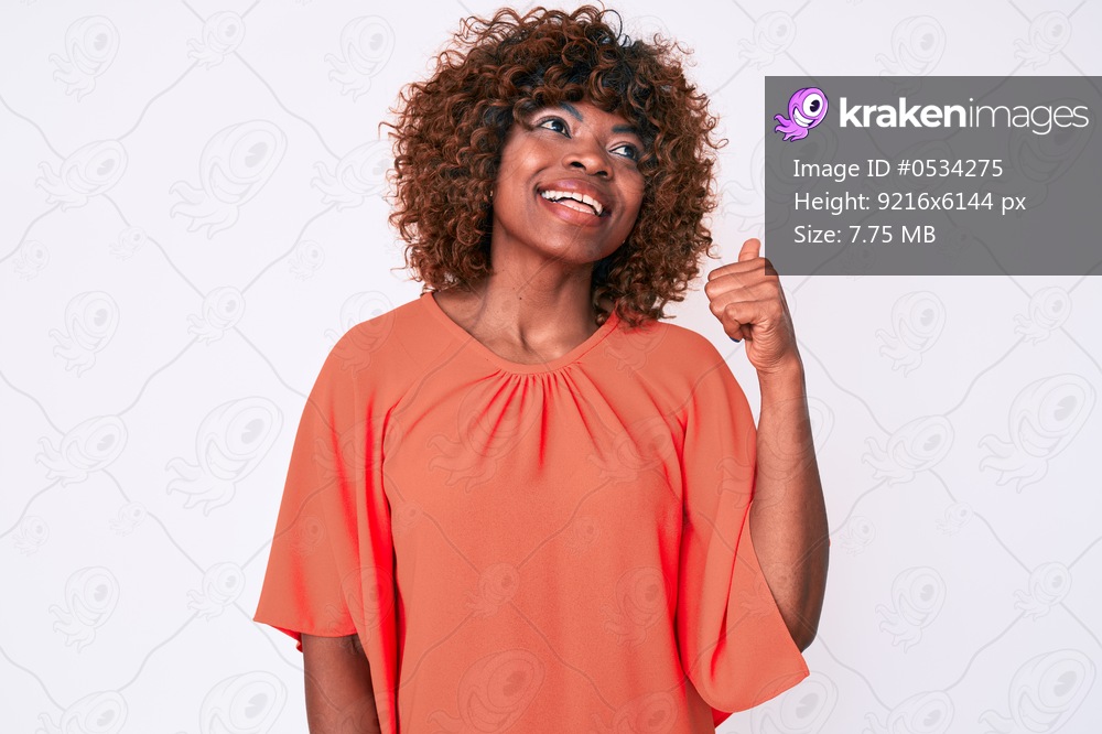 Young african american woman wearing casual clothes smiling with happy face looking and pointing to the side with thumb up. 
