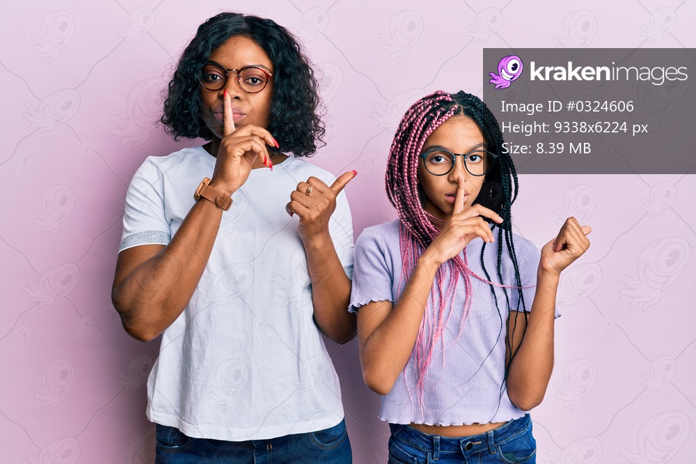 Beautiful african american mother and daughter wearing casual clothes and glasses asking to be quiet with finger on lips pointing with hand to the side. silence and secret concept. 
