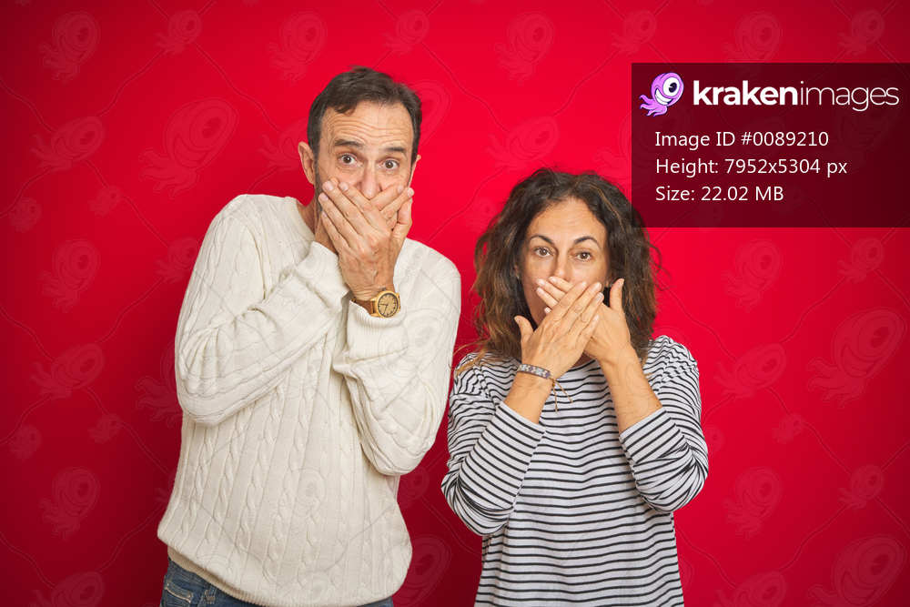 Beautiful middle age couple wearing winter sweater over isolated red background shocked covering mouth with hands for mistake. Secret concept.