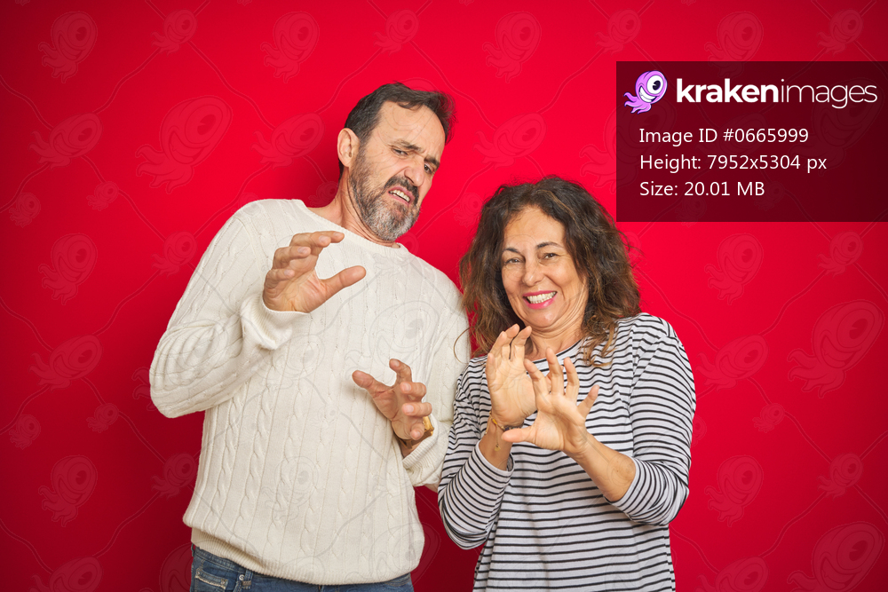 Beautiful middle age couple wearing winter sweater over isolated red background disgusted expression, displeased and fearful doing disgust face because aversion reaction. With hands raised. Annoying concept.