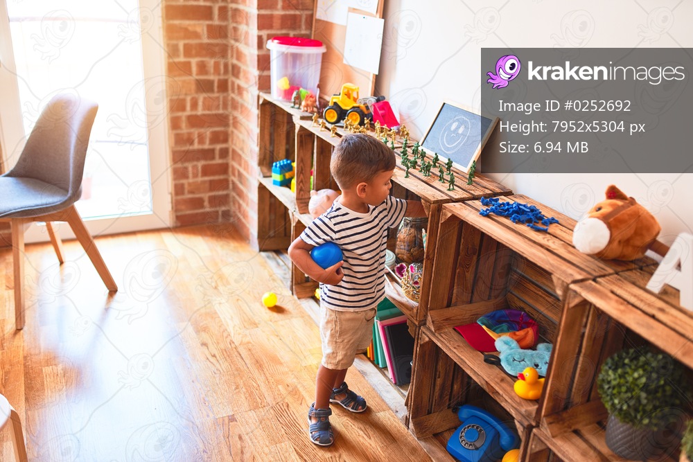 Beautiful toddler boy playing with colored small balls at kindergarten