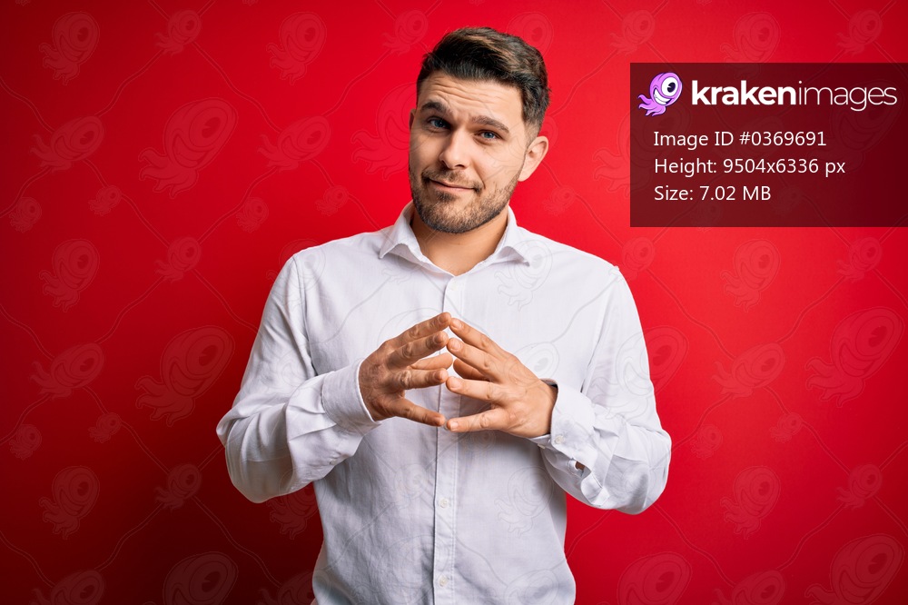 Young business man with blue eyes wearing elegant shirt standing over red isolated background Hands together and fingers crossed smiling relaxed and cheerful. Success and optimistic