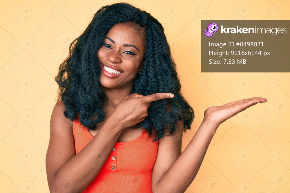 Beautiful african woman wearing casual clothes amazed and smiling to the camera while presenting with hand and pointing with finger. 