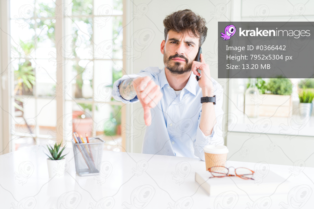 Young business man talking on smartphone with angry face, negative sign showing dislike with thumbs down, rejection concept