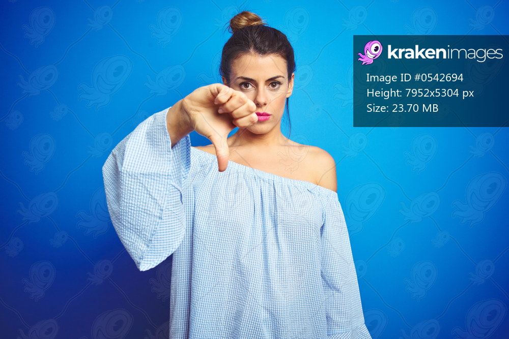 Young beautiful woman wearing bun hairstyle over blue isolated background looking unhappy and angry showing rejection and negative with thumbs down gesture. Bad expression.