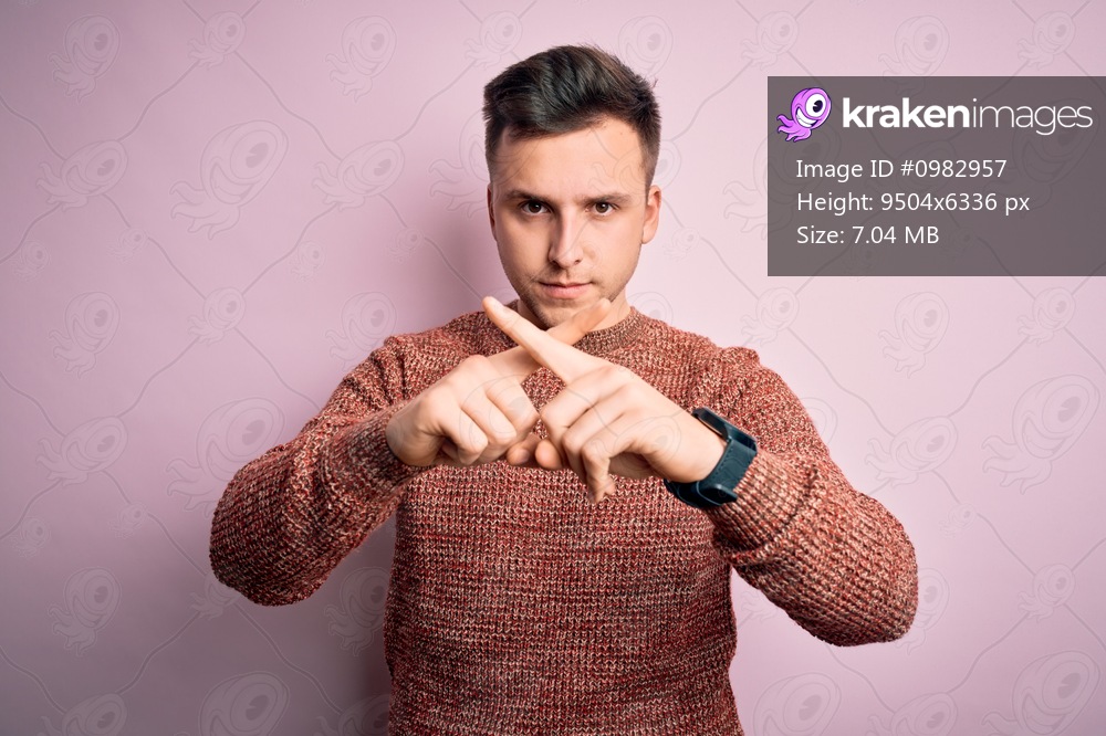 Young handsome caucasian man wearing casual winter sweater over pink isolated background Rejection expression crossing fingers doing negative sign