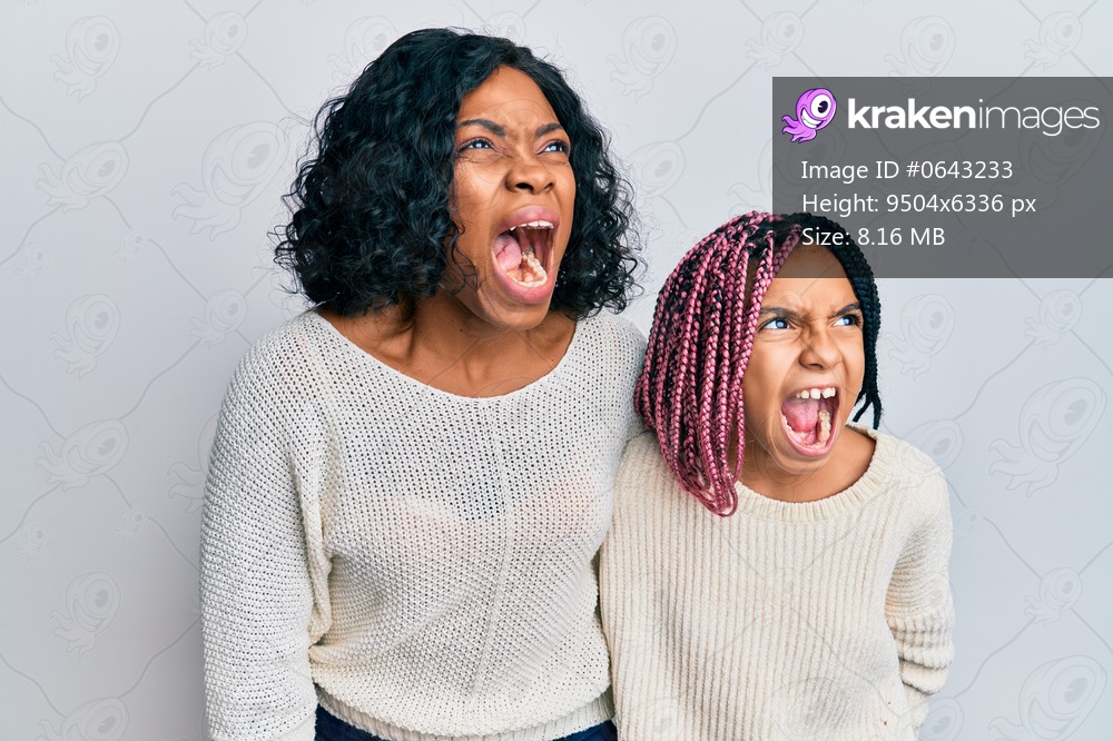 Beautiful african american mother and daughter wearing casual clothes and hugging angry and mad screaming frustrated and furious, shouting with anger. rage and aggressive concept. 