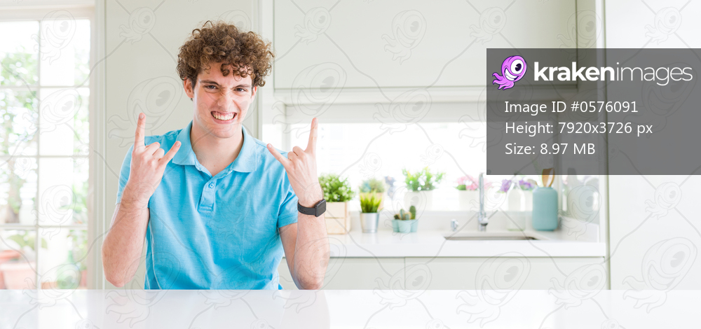 Wide shot of young handsome man at home shouting with crazy expression doing rock symbol with hands up. Music star. Heavy concept.