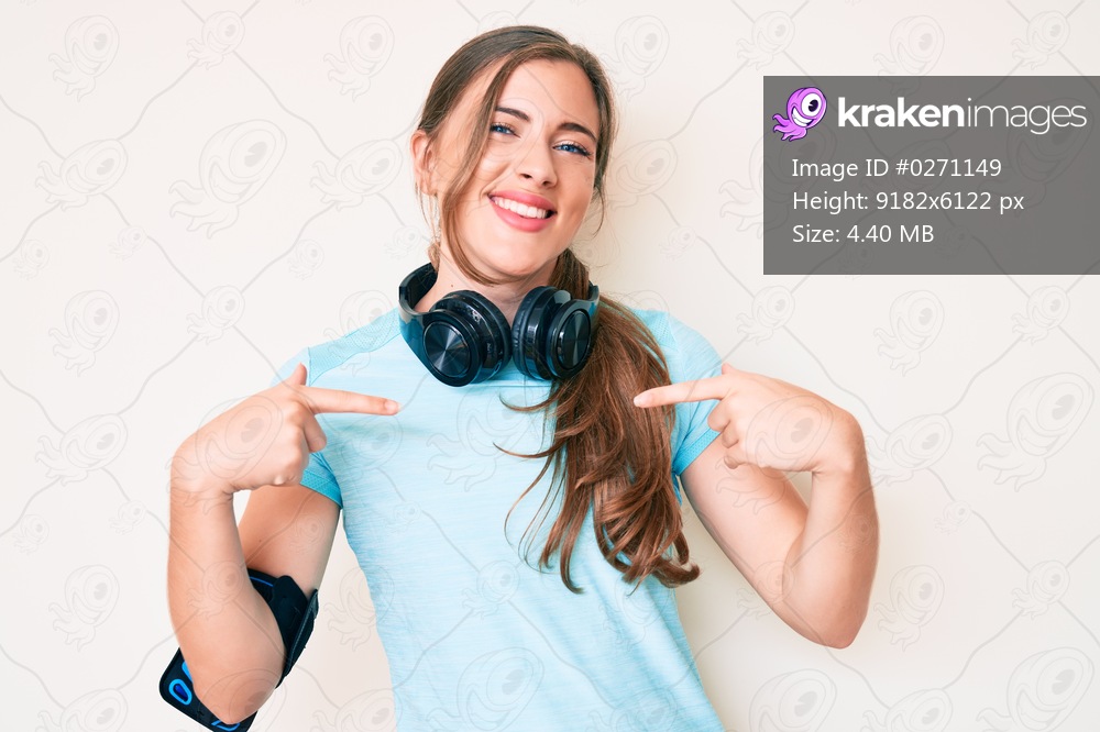Beautiful young caucasian woman wearing gym clothes and using headphones looking confident with smile on face, pointing oneself with fingers proud and happy. 