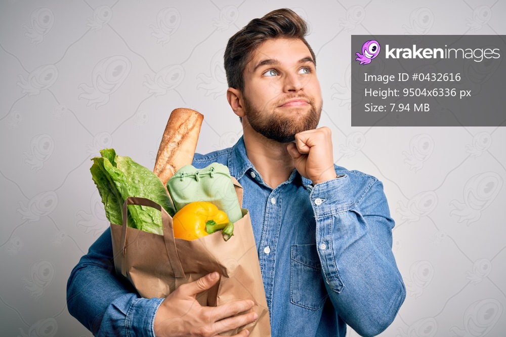 Young blond man with beard and blue eyes holding paper bag with food over white background serious face thinking about question, very confused idea
