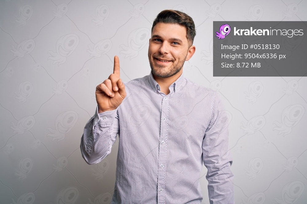 Young business man with blue eyes standing over isolated background showing and pointing up with finger number one while smiling confident and happy.