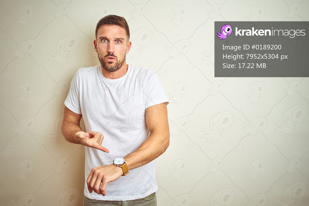 Young handsome man wearing casual white t-shirt over isolated background In hurry pointing to watch time, impatience, upset and angry for deadline delay