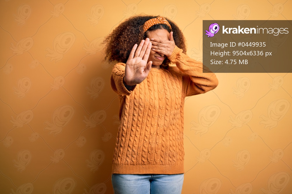 Young african american woman with afro hair wearing casual sweater over yellow background covering eyes with hands and doing stop gesture with sad and fear expression. Embarrassed and negative concept.