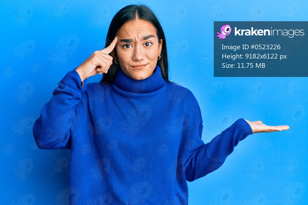 Young asian woman wearing casual winter sweater confused and annoyed with open palm showing copy space and pointing finger to forehead. think about it. 