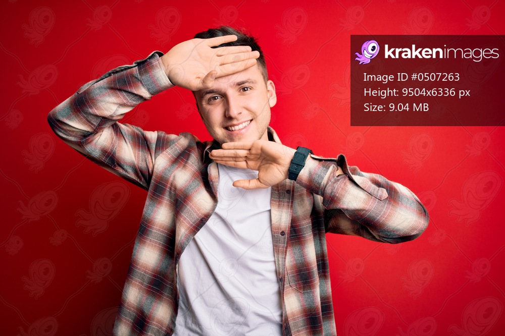 Young handsome caucasian man wearing casual modern shirt over red isolated background Smiling cheerful playing peek a boo with hands showing face. Surprised and exited