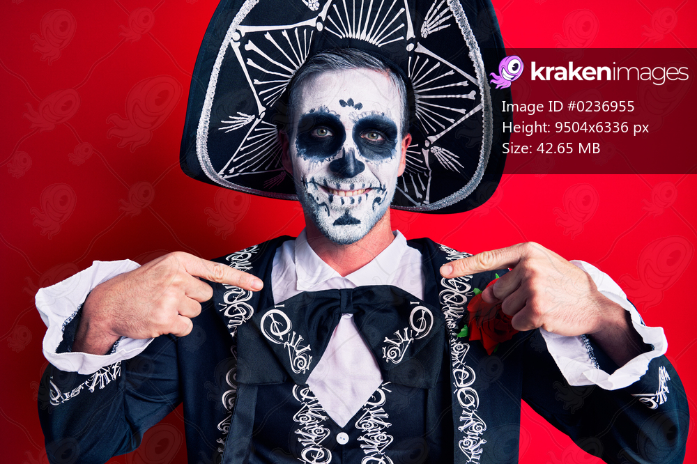 Young man wearing mexican day of the dead costume over red looking confident with smile on face, pointing oneself with fingers proud and happy. 