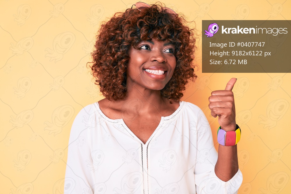 Young african american woman wearing casual clothes smiling with happy face looking and pointing to the side with thumb up. 