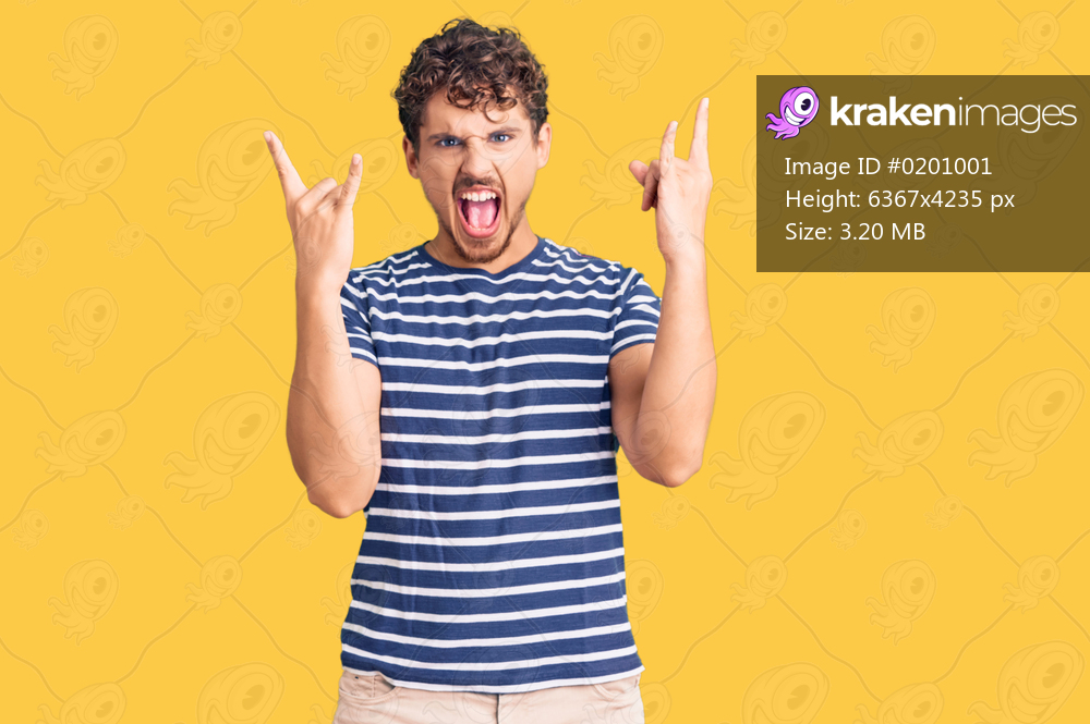 Young handsome man with curly hair wearing casual clothes shouting with crazy expression doing rock symbol with hands up. music star. heavy concept. 