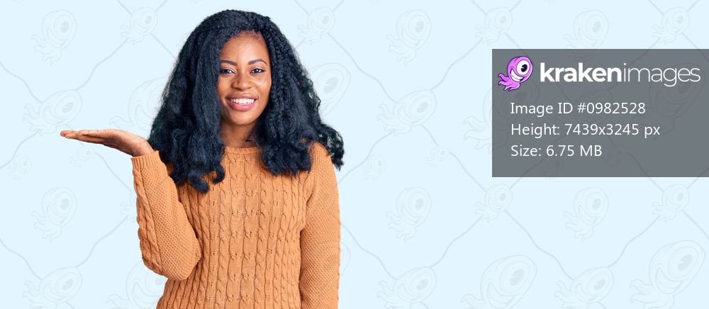 Beautiful african american woman wearing casual  sweater smiling cheerful presenting and pointing with palm of hand looking at the camera. 