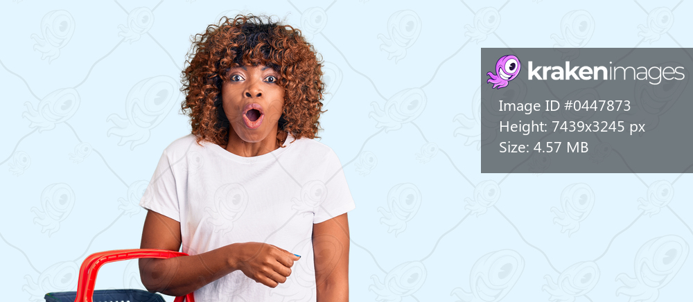 Young african american woman holding supermarket shopping basket scared and amazed with open mouth for surprise, disbelief face 
