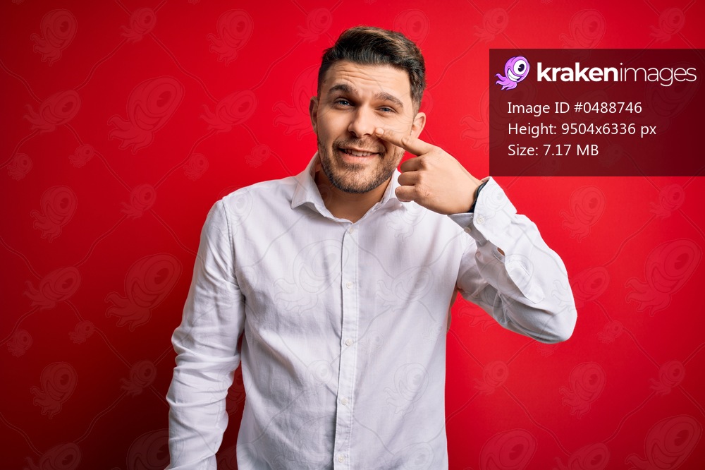 Young business man with blue eyes wearing elegant shirt standing over red isolated background Pointing with hand finger to face and nose, smiling cheerful. Beauty concept