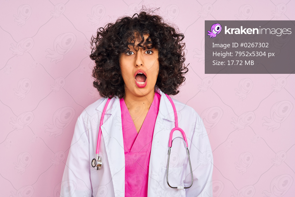 Young arab doctor woman with curly hair wearing stethoscope over isolated pink background afraid and shocked with surprise expression, fear and excited face.