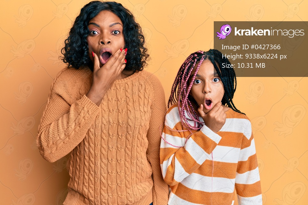 Beautiful african american mother and daughter wearing wool winter sweater looking fascinated with disbelief, surprise and amazed expression with hands on chin 