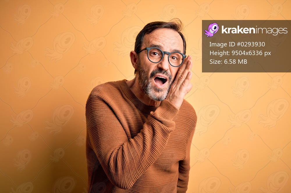 Middle age hoary man wearing brown sweater and glasses over isolated yellow background hand on mouth telling secret rumor, whispering malicious talk conversation