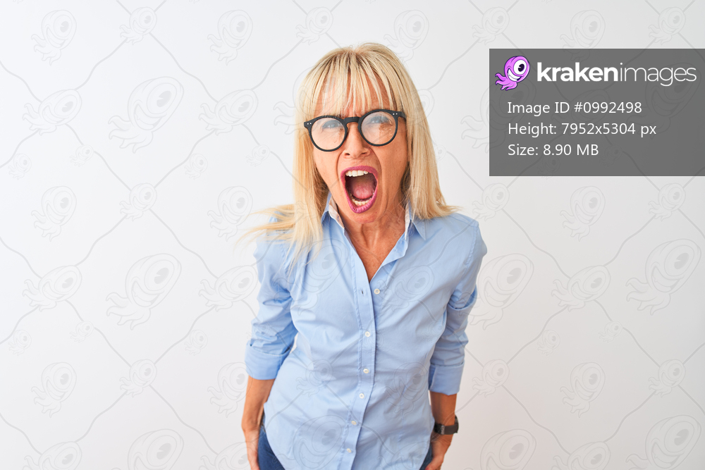 Middle age businesswoman wearing elegant shirt and glasses over isolated white background angry and mad screaming frustrated and furious, shouting with anger. Rage and aggressive concept.