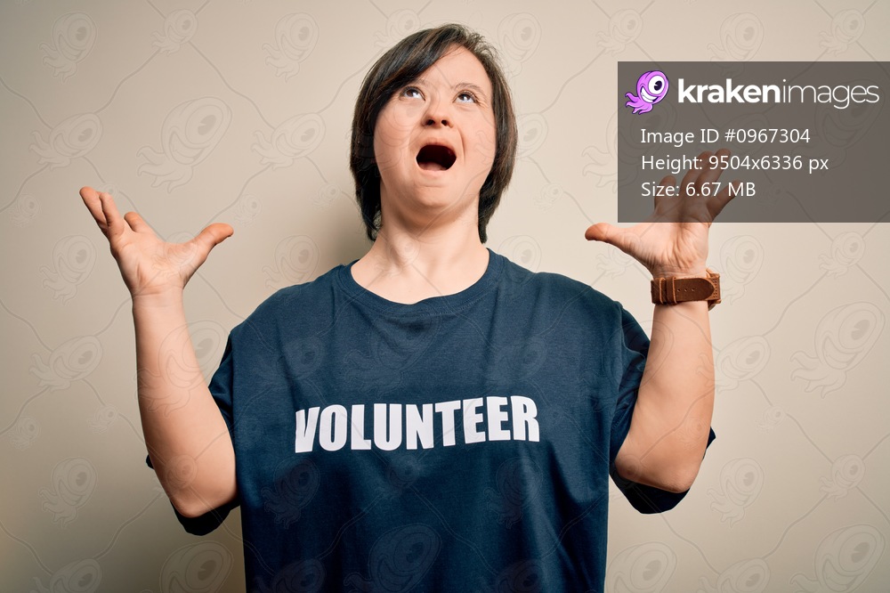 Young down syndrome volunteer woman wearing social care charity t-shirt crazy and mad shouting and yelling with aggressive expression and arms raised. Frustration concept.
